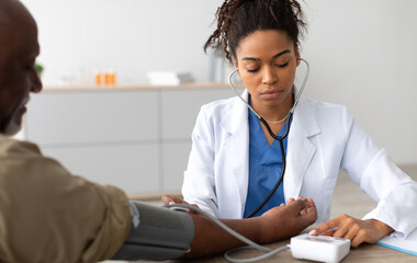 Young Focused African American Lady Examining Older Patient Measuring Arterial Blood Pressure With...