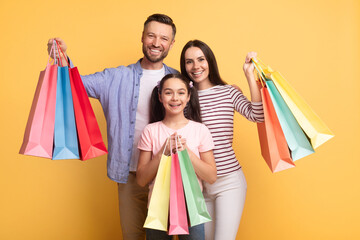 A cheerful family consisting of a mother, father, and teenage daughter poses happily, holding colorful shopping bags. They display love and connection in a vibrant setting.