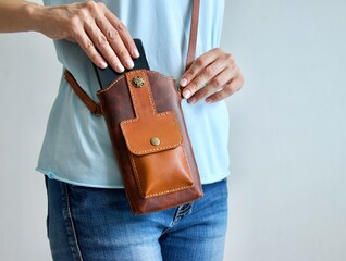 Close-up of female hands take smartphone out of small leather crossbody bag. Unrecognizable woman opens calfskin handbag. Communication and lifestyle concept.