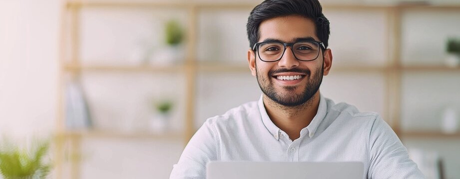 Friendly young man smiling at laptop in a bright office setting - Powered by Adobe