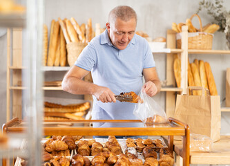 Mature man customer puts freshly baked croissants in plastic bag in bakery