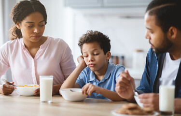 A mother and father share a meal with their son in a warm kitchen. The family is engaged in conversation, showcasing love and connection during their breakfast routine.