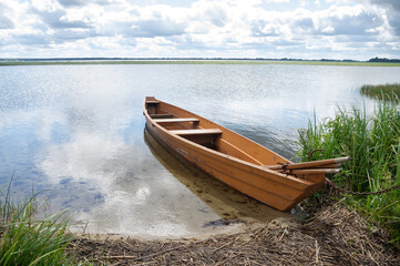 A wooden boat with oars moored at the shore of a lake.