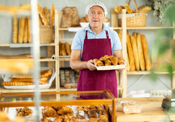 Mature man seller holding basket with fresh croissants in bakery