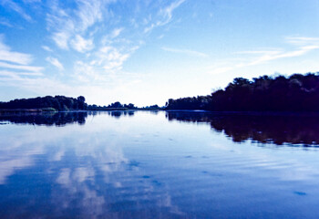 Silhoetted tree line reflected on a lake in the evening blue light.