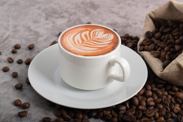 Cup of coffee latte with art shape and coffee beans on dark cement background.