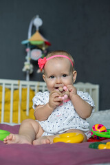 A cheerful baby girl sits on a soft surface, surrounded by colorful toys. She is playfully grasping a teething ring with delight in her eyes, radiating happiness in her playful world.