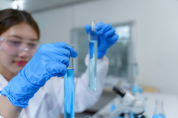 Scientist wearing blue gloves and safety glasses comparing two test tubes with blue liquid in a laboratory setting