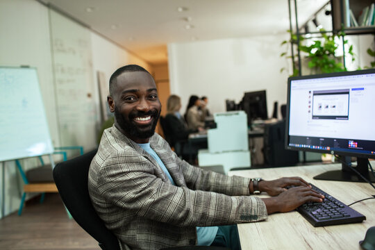 Portrait of a smiling businessman working at office computer - Powered by Adobe