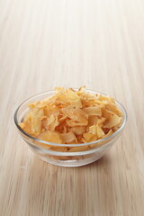 Cassava chips in a clear glass bowl on a plywood base photographed with studio light