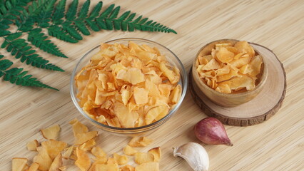 Cassava chips in a clear glass bowl on a plywood base photographed with studio light