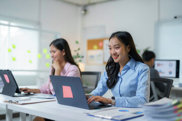 Young asian businesswoman smiling and working with laptop computer at office desk with colleagues