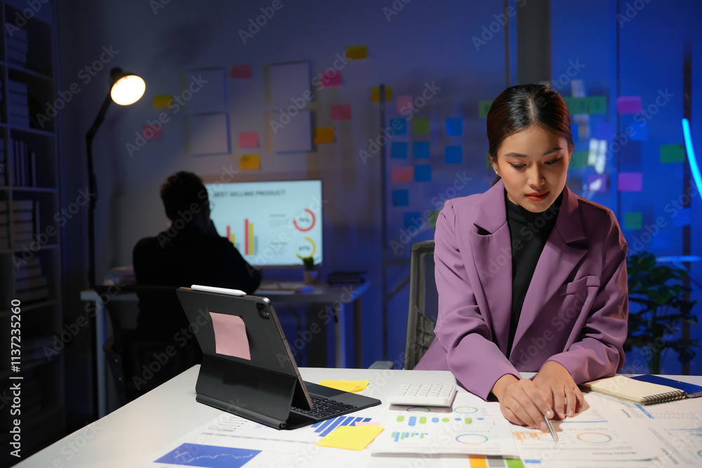 Poster young manager reviewing marketing data and graphs on paperwork, using tablet and computer, working o