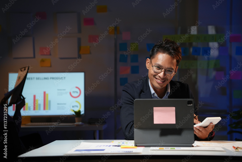 Aufkleber smiling asian businessman working late in office using calculator and tablet with sticky notes on wa