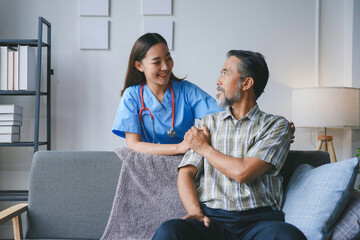 Fototapeta premium Smiling nurse is assisting elderly patient sitting on sofa, providing medical care and support at his residence