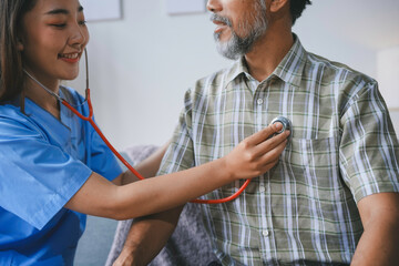 Smiling nurse using stethoscope examining heartbeat of senior patient during home visit, providing...