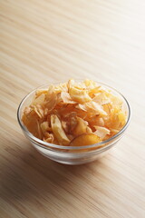 Cassava chips in a clear glass bowl on a plywood base photographed with studio light
