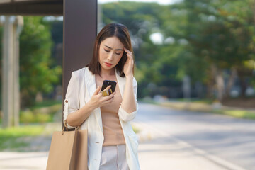 Asian businesswoman holding shopping bags and a credit card having problems with mobile banking...