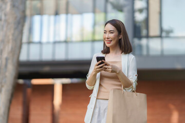 Fototapeta premium Happy businesswoman using a smartphone and holding a shopping bag, enjoying shopping and connectivity