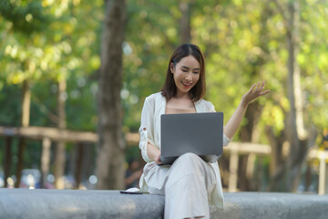 Asian businesswoman using laptop for video conference, working remotely in a park, enjoying work life balance