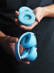Blue headphones held in hands against a dark background, showcasing changing replacement ear pads ear cushion.