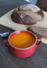 Freshly made tomato soup in a red ceramic bowl on a wooden dining table