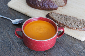Freshly made tomato soup in a red ceramic bowl on a wooden dining table