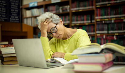 Elderly woman sitting in a library, combining traditional and modern approaches to learning or research by book and laptop computer sense of purpose dedication to personal grown concept.