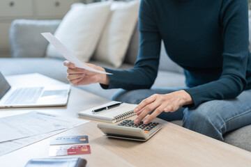 Stressed asian young business woman, employee using calculator to calculate expenses of monthly, hand holding bills and receipt for to payment on table at home. Financial, finance of banking concept.