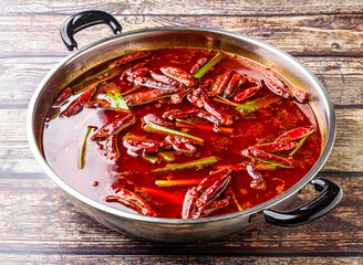 Spicy Sichuan hotpot with chili peppers and scallions served in steel pot isolated on wooden table side view of hong kong food