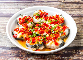 Steamed white eel with chopped pepper served in bowl isolated on wooden table side view of hong kong food