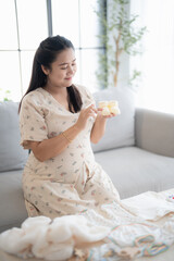 Pregnant asian woman getting ready for the maternity hospital preparing and planning baby clothes for new baby of pregnancy packing baby stuff on bed.