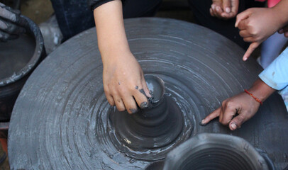 Children's hands shaping clay on a pottery wheel, showcasing teamwork, creativity, and hands-on...