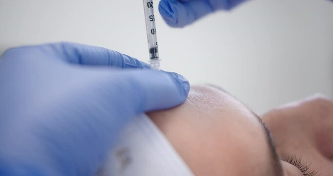 Amazing close-up and slow motion shot of a botox injection being injected into the forehead of a young man for a rejuvenation treatment in a dermatology clinic