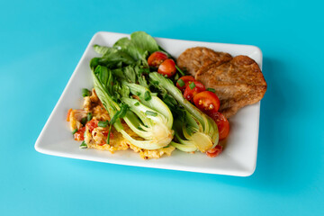 Fresh bok choi is served alongside vegetarian meat and juicy tomatoes on a vibrant plate.