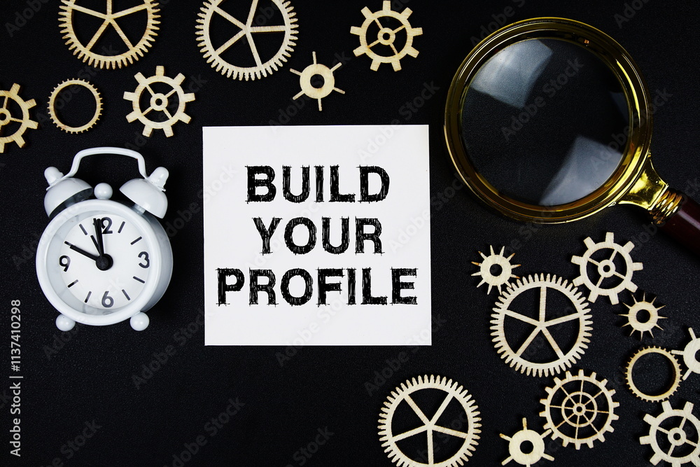 Aufkleber build your profile text message on sticky note with magnifying glass and alarm clock on black backgr