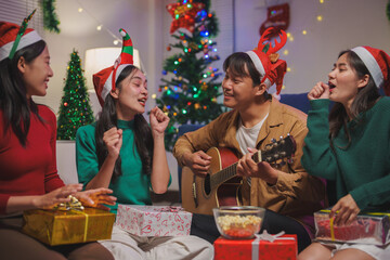 Group of young Asian friends celebrate Christmas Eve enjoying singing and playing guitar at a house party..Have fun while having fun clapping together in happiness, cheerfulness, celebration concept.