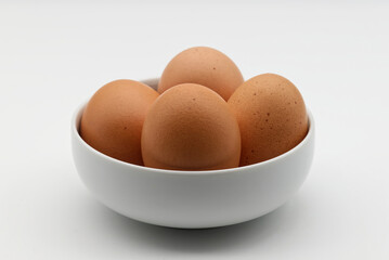 Close-up of four brown eggs nestled in a simple white bowl against a plain white background.