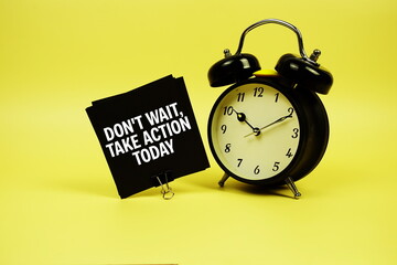 Don't Wait, Take Action Today text message on sticky note with alarm clock on yellow background