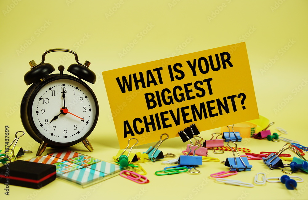 Poster what is your biggest achievement? text on paper card with alarm clock and stationery on yellow backg