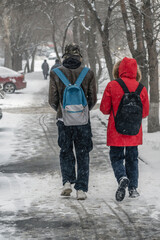 People with backpacks walk along a snow-covered sidewalk on a winter day