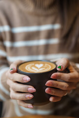 young woman drinking cappuccino with heart latte art in winter, female with Christmas Nail art manicure and hand holding and enjoying a cup of coffee at home in the morning