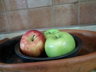 Two green apples and one red apple resting in black clay bowl