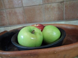 Two green apples and one red apple resting in black clay bowl
