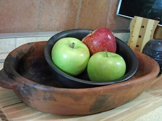 Two green apples and one red apple resting in black clay bowl