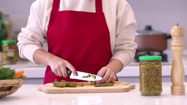 Close up view of male hands chopping cucumber on wooden cutting board with knife	

