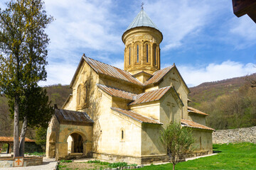 Church in the courtyard of the Kvatakhevi monastery. Stone walls, tiled roof. Stone paths, green grass, bright blue sky.