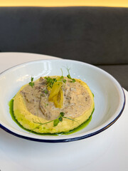 A creamy, savory dish of stew on mashed potatoes garnished with pickles and greens, served in soft natural light, ideal for cozy winter dining