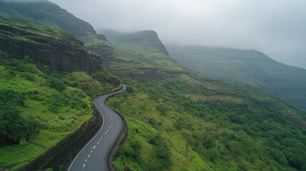 Fototapeta premium Winding road through lush, misty green mountains.