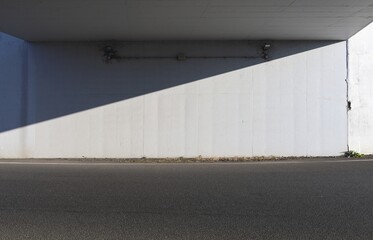 White concrete wall of a road underpass divided in two by the shadow of the bridge. Two lamps on top and street in front. Background for copy space	